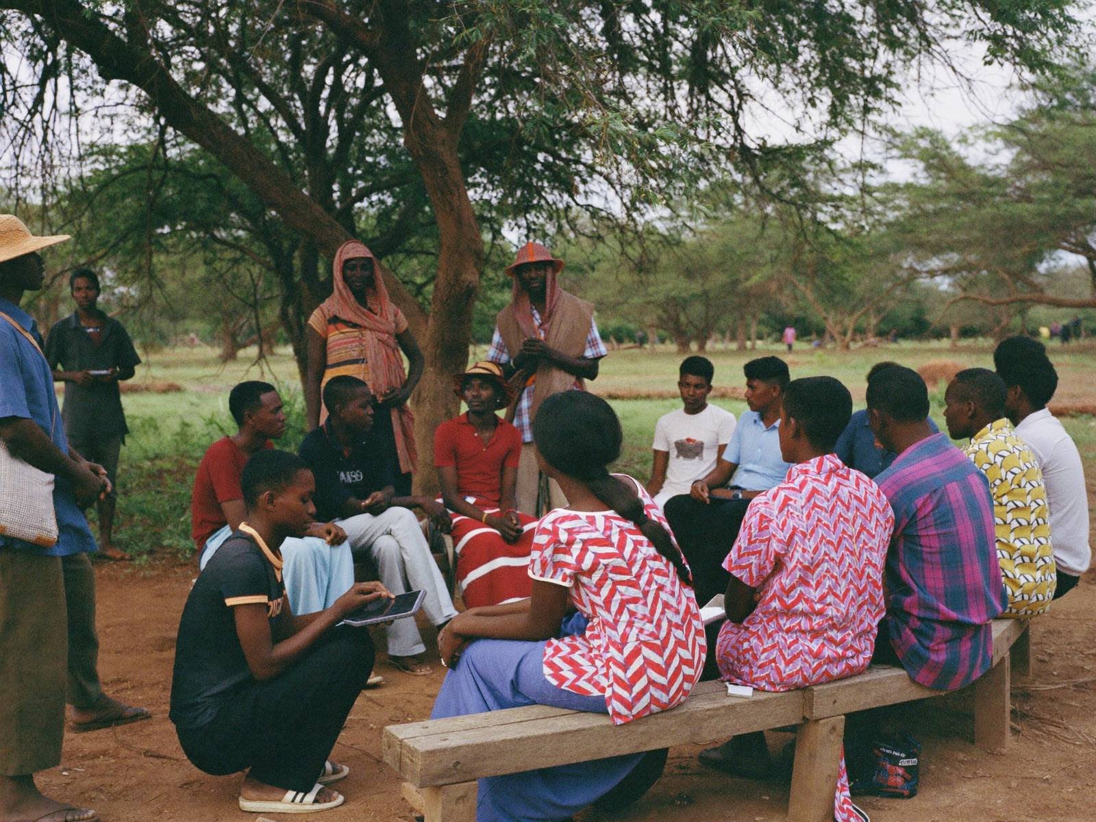 Enumerator listening to a community focus group under an acacia tree